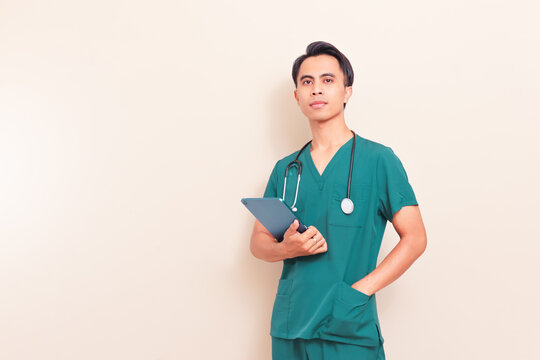 Smiling Southeast Asian male nurse or doctor in green scrubs holding a digital tablet. Professional healthcare worker presenting medical information or digital records on isolated background.