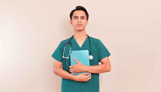 Smiling Southeast Asian male nurse or doctor in green scrubs holding a digital tablet. Professional healthcare worker presenting medical information or digital records on isolated background.