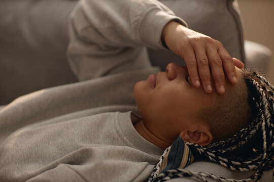 Close up of young adult woman resting on sofa, covering forehead and coping with stress during house arrest. Suitable for mental health, isolation, burnout, lockdown campaigns