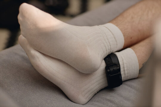 Close up of young adult man wearing electronic ankle monitor during house arrest, showing legal surveillance and restricted freedom. Useful for crime, justice, probation campaigns
