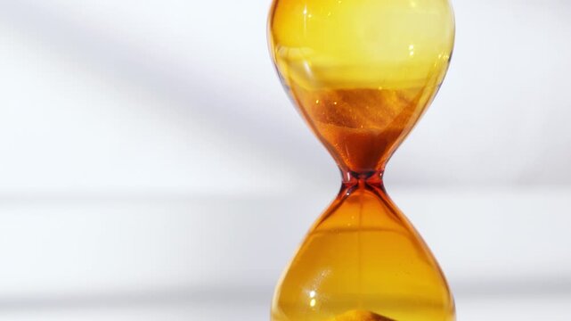 Close-up of Amber Hourglass with Sand Falling on White Background - Concept of Time