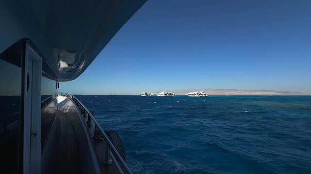 Yacht tint window and deck floating in Red Sea with distant anchored boats under clear sky