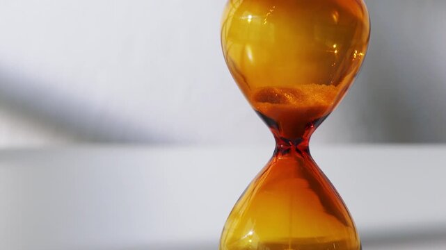 Close-up of Amber Hourglass with Sand Falling on White Background - Concept of Time Passing