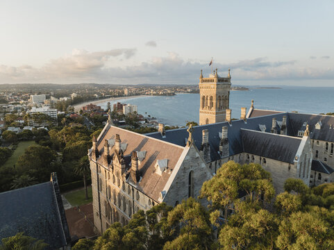 Aerial view of the International College of Management, Sydney featuring its historic stone architecture and tower overlooking Manly Beach and the ocean in Manly, New South Wales, Australia.