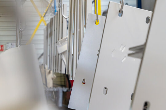 S&eacute;rie de panneaux et profil&eacute;s m&eacute;talliques blancs suspendus &agrave; un convoyeur a&eacute;rien industriel pour le traitement de surface ou le s&eacute;chage en usine.