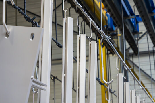 Vue align&eacute;e de profil&eacute;s m&eacute;talliques blancs suspendus verticalement &agrave; un rail de convoyage automatis&eacute; pour le traitement de surface en usine.