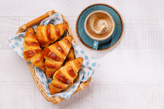 Aromatic croissants in wicker basket with cup of coffee