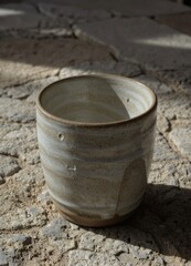Naklejka premium Ceramic cup with textured glaze on stone surface in sunlight