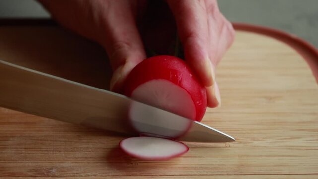 Close-Up of Woman's Hands Thinly Slicing Fresh Radishes on a Wooden Cutting Board