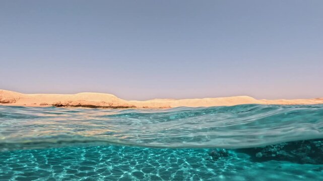 Slow motion half underwater view of sandy seabed coral reef and desert coast of Red Sea