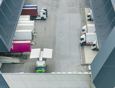 Aerial view of semi-trucks and colorful shipping containers parked at a logistics distribution center with loading docks and warehouse roofs Taiwan.