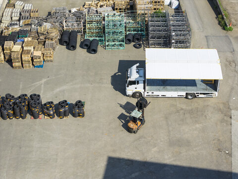 Aerial view of a white logistics truck and a person operating a forklift in an industrial yard with stacks of tires and wooden pallets in Taiwan.