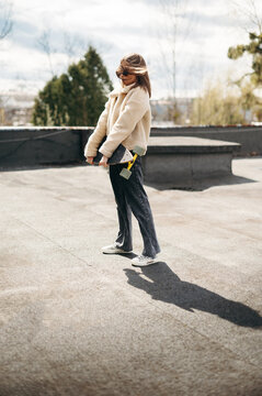 Stylish woman holding skateboard while standing on roof