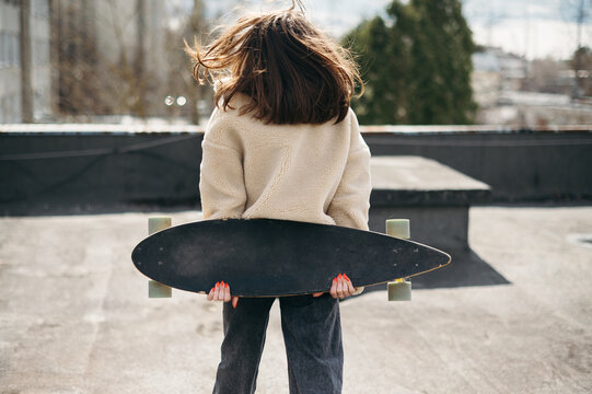 Back view of young brunette posing with skateborad on roof