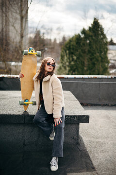 Young woman in stylish wear posing on roof with skateboard