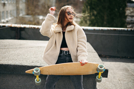 Pretty woman sitting with skateboard on sunlight rooftop