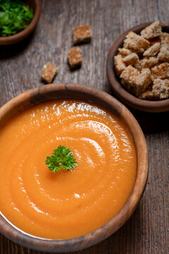 Cremate carrot soup  on a rustic wooden table  croutons on the side.