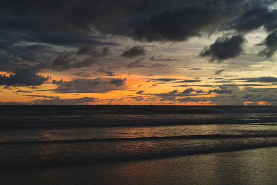 Dramatic orange sunset over dark ocean waves, Canggu, Bali