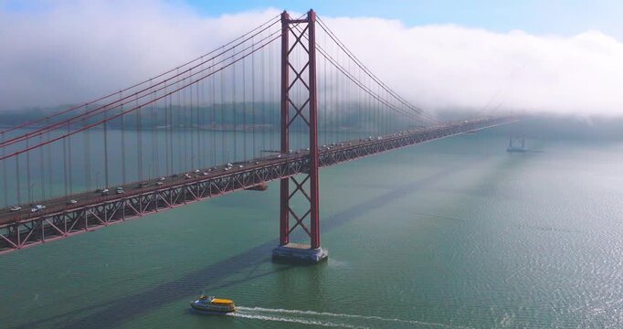 Aerial establishing shot of the 25th April Bridge over the Tagus River, with clouds and fog over the bridge in Lisbon, Portugal