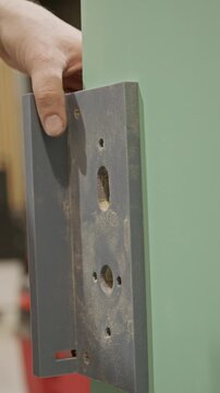 Close-up vertical shot of a carpenter removing a mortise lock template from a
door after completing the drilling process. The pre-cut holes for the lockset are visible, highlighting precise alignment.