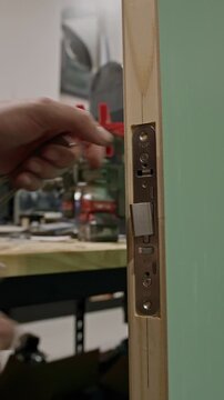 Vertical close-up of a craftsman carefully positioning and installing a metal mortise lock faceplate into a recessed wooden door edge.