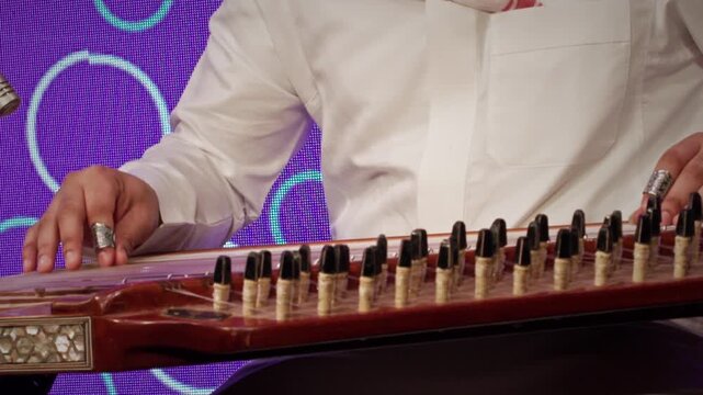 A musician in traditional Saudi attire playing the qanun, a classical
Middle Eastern string instrument. The performer&rsquo;s hands skillfully pluck the
strings using finger picks.