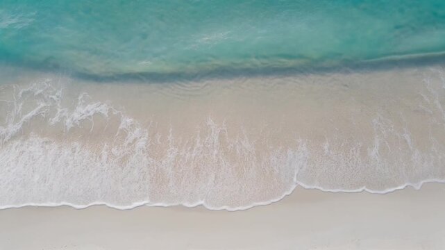 Aerial view of turquoise ocean waves gently washing onto a sandy beach on a sunny day