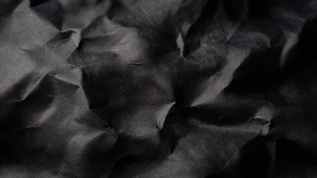 Close up of crumpled black paper texture background with dark shadows and highlights