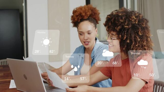 Two colleagues sitting at table tapping laptop, animated weather cards sliding across documents
