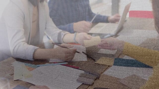 Left woman handing teal swatch, team pairing samples, tapping tablet, finalizing design materials
