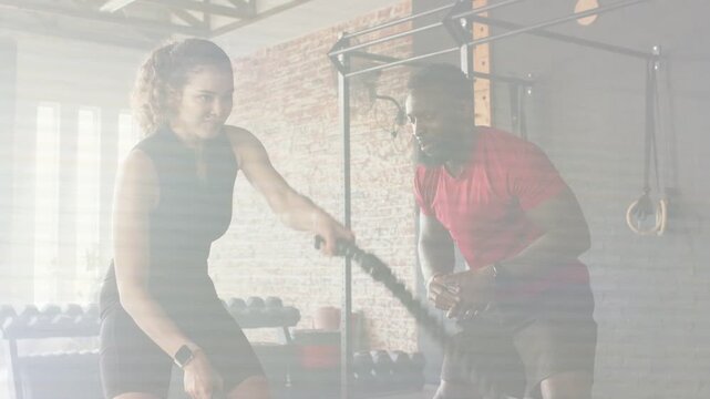 Trainer clapping and cueing while woman performing alternating-wave battle rope in gym for form