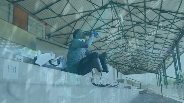 Teenage male sitting on bleachers grabbing blue water bottle hydrating after sports surveying field