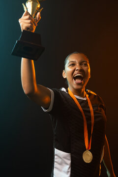African American woman raising gold cup with b and w jersey gold medal orange ribbon studio teal or 