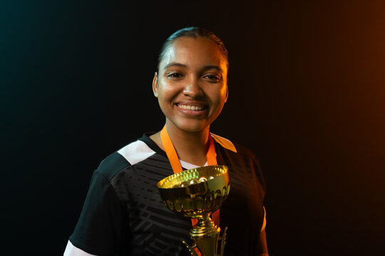 African American woman holding gold trophy cup in studio wearing black jersey with teal rim lights