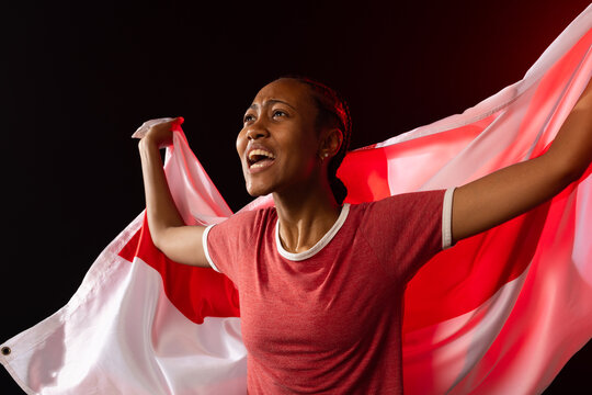African American woman in red ringer tee shouting and holding flag with red cross in studio