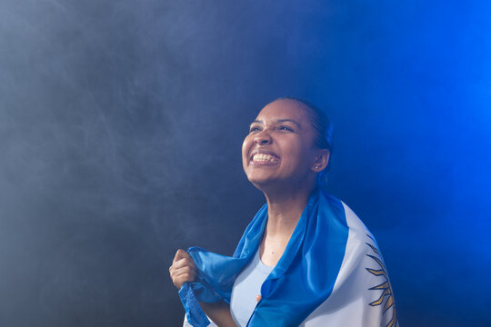 Female in tank top holding blue-and-white sun-emblem flag, grinning in fog, blue light, copy space