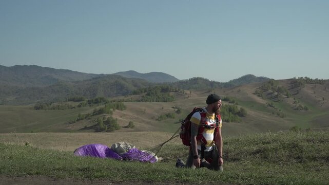 Skydiver after landing in wilderness area. Tired pilot enjoying extreme sports stands on his knees. Adrenaline, risk, challenges.