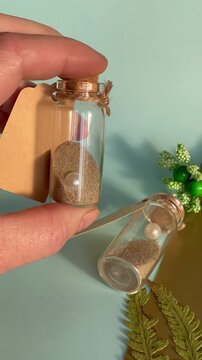Hand holding small glass souvenir bottle with sea sand pearl and craft tag, wedding favors and summer memory concept