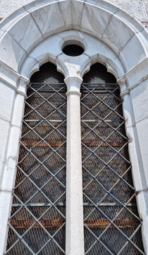 An ornate neo Gothic bifora window with stone carvings and metal protective mesh on the facade of the Capuchin Church of Our Lady of Lourdes in Rijeka