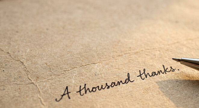 A thousand thanks handwritten note on textured brown paper with a pen resting.