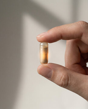 Macro shot of a hand holding a transparent capsule with a glowing core. Symbolizing advanced bioavailability and high-tech nutritional supplementation.