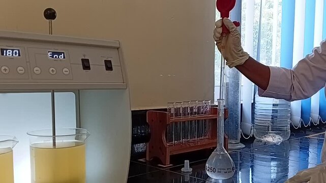 Technician in Lab Coat Using Glass Pipette and Pump Driver for Precise Chemical Measurement in Jar Test