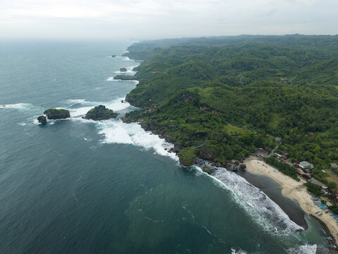 Aerial view of Siung Beach with its white sand, dramatic limestone cliffs, and turquoise waves crashing against the rocky shore in Tepus, Special Region of Yogyakarta, Indonesia.