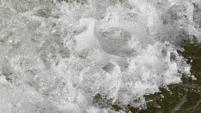 Sparkling white foam and bubbles churn energetically in a fast river. The lively movement of the water creates a refreshing and powerful feeling of pure natural energy.