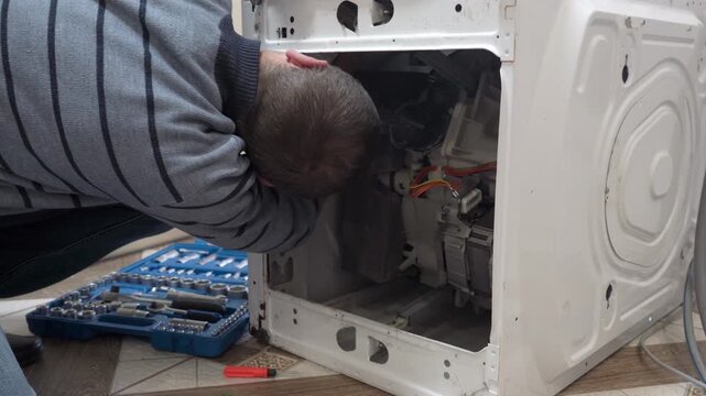 Technician repairing washing machine with a toolkit, A man bent over a disassembled washing machine, repairing internal components. home appliance service, professional home help and technical experti