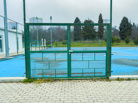 Tennis court with green gate and blue surface in an urban area during a cloudy day