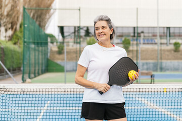 Happy senior woman holding a pickleball paddle and ball, actively enjoying sports and a healthy retirement lifestyle © Koldo_Studio