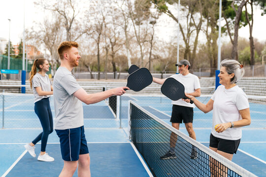 Group of diverse age adults smiling, interacting, and playing pickleball together on a blue court, enjoying a fun sport