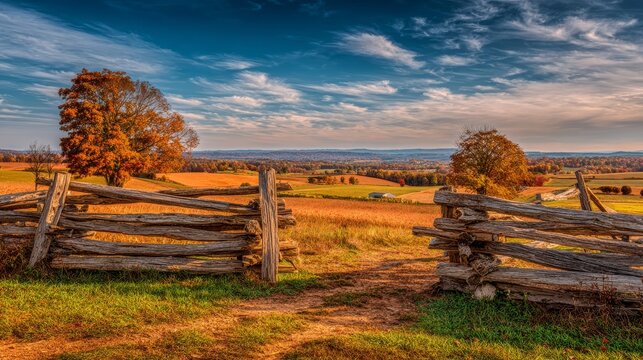Rustic split rail wooden fence marking the entrance to an expansive autumn countryside landscape with rolling fields under a dramatic sky