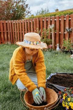 Child adding compost while planting flowers in garden container